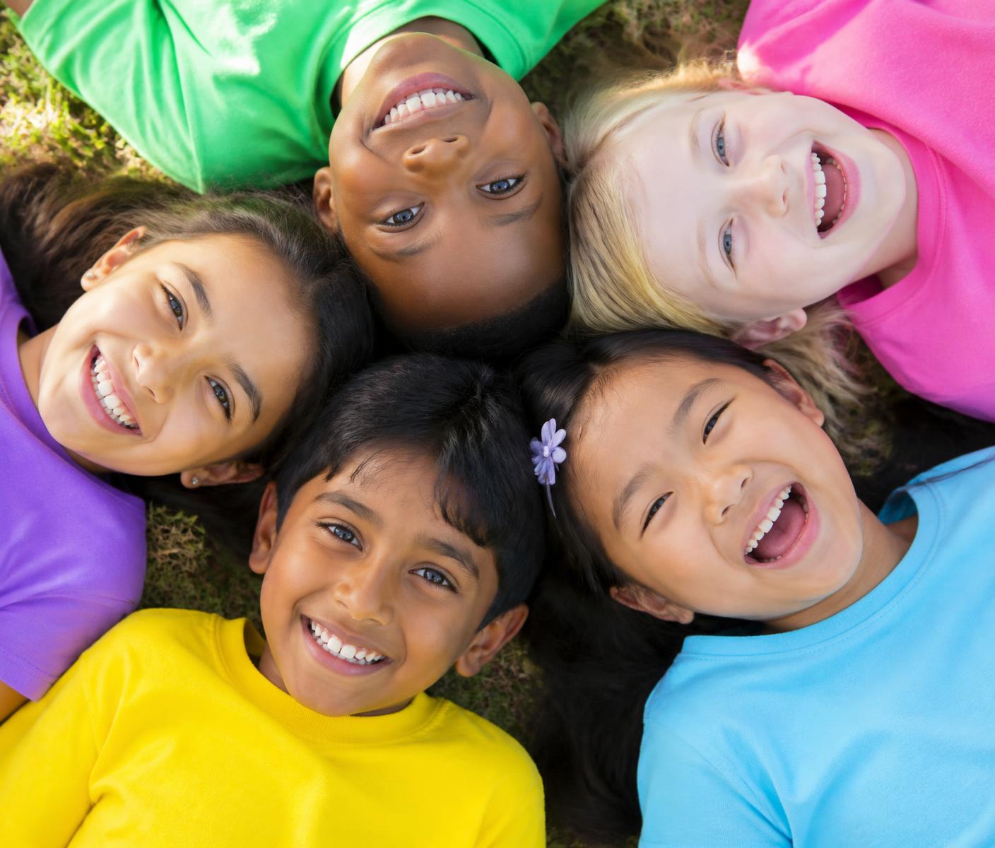 Five smiling children of diverse backgrounds and skin tones lying in a circle looking up